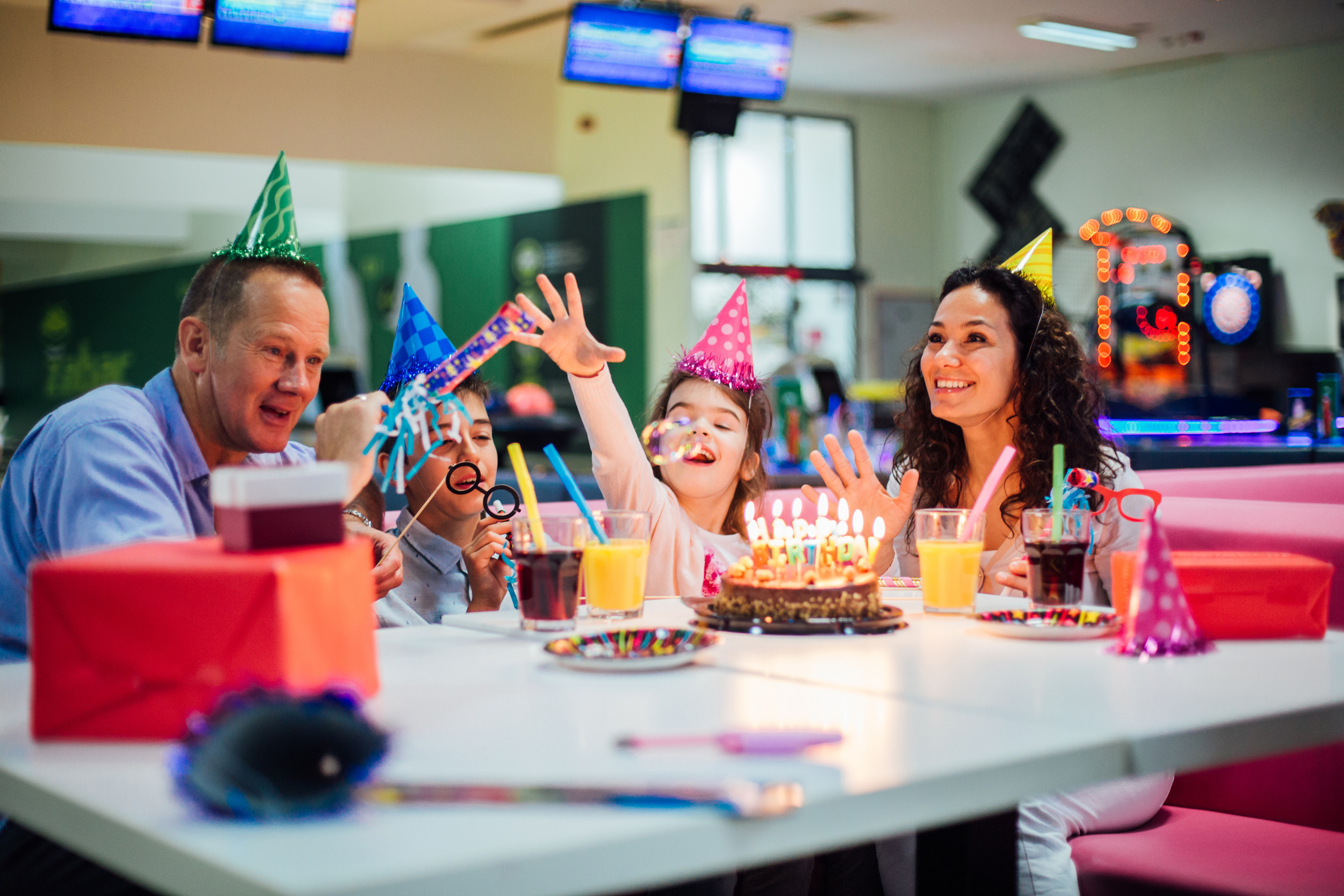 Kinder feiern fröhlich einen Geburtstag in einer Bowlingbahn mit Kuchen und Geschenken.