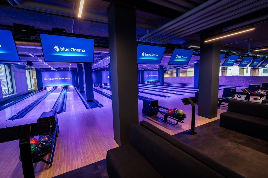 Blick auf Bowlingbahnen mit bequemen Sitzgelegenheiten und blauer Beleuchtung.