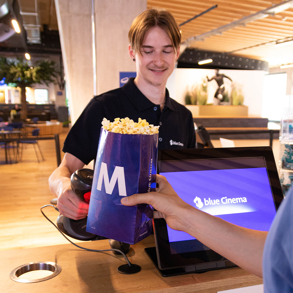 A smiling staff member at blue cinema holding a tray with popcorn.