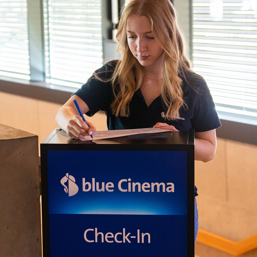 Ein Teammitglied im blue cinema bei der Registrierung einer Buchung am Check-In Schalter.