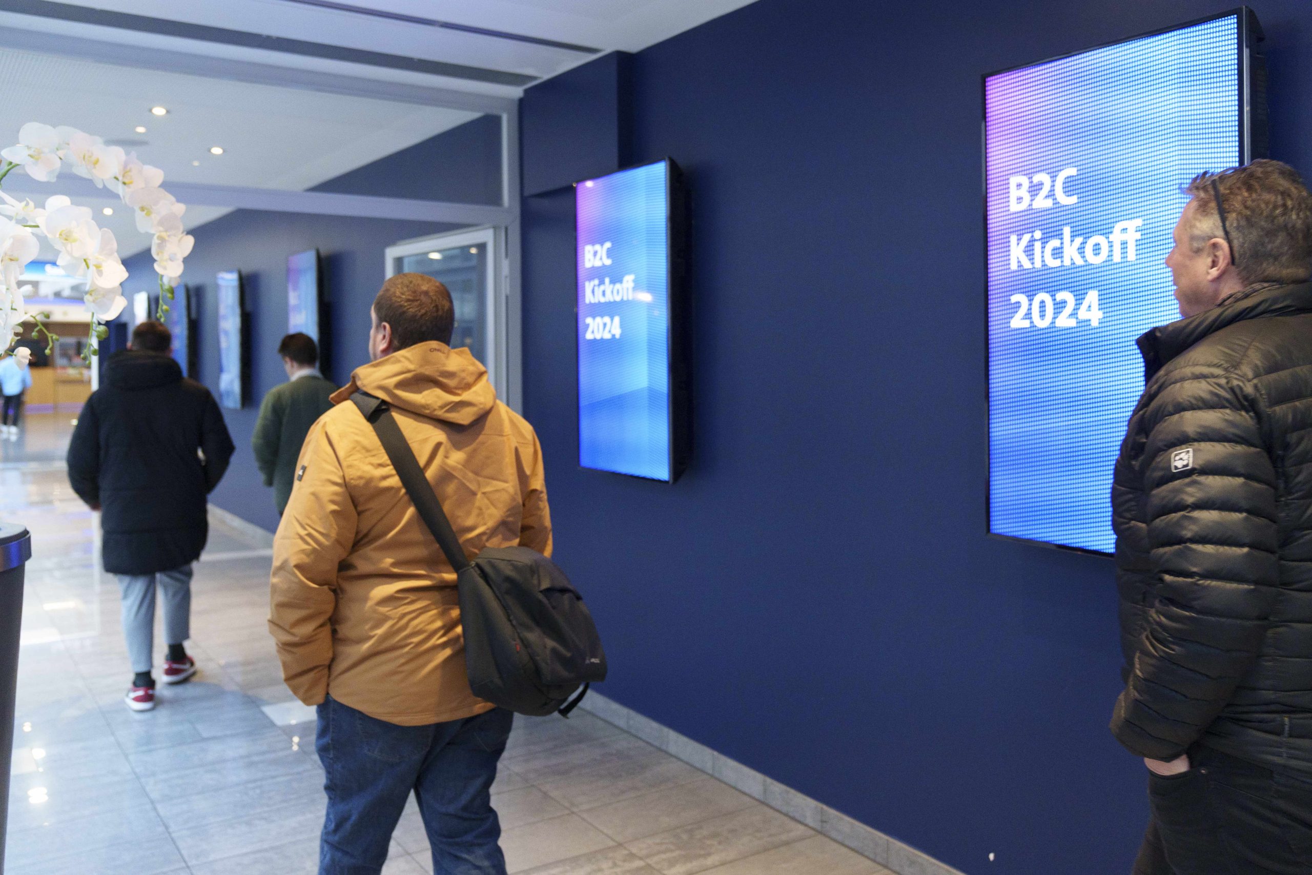 Des visiteurs regardent un panneau publicitaire numérique annonçant "B2C Kickoff 2024" dans le hall du cinéma.